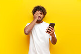 young indian sad guy using smartphone online with facepalm on yellow isolated background