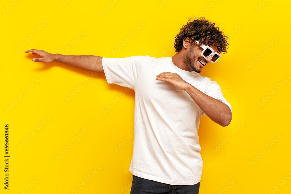young indian guy in sunglasses dancing dab on yellow isolated background, south asian man in white t-shirt - obrazy, fototapety, plakaty 