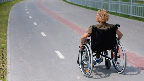 Rear view of an elderly woman in a wheelchair riding on a bike path. 