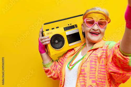 funny old granny with tape recorder in sports hipster clothes takes selfie online on yellow isolated background