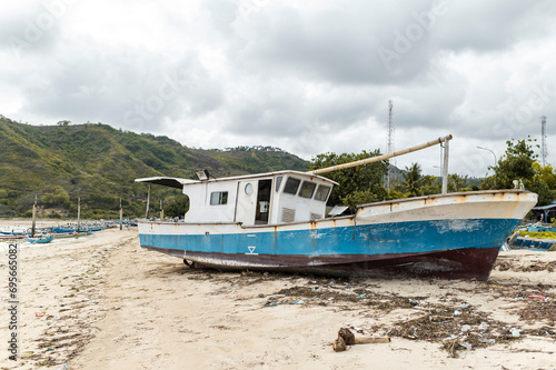 Abandoned blue and white fishing boat rests on sandy beach under a clouded sky, Indonesia, Asia photo
