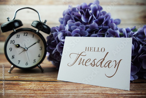 Hello Tueday text mesage with alarm clock and purple hydragea flower on wooden background photo