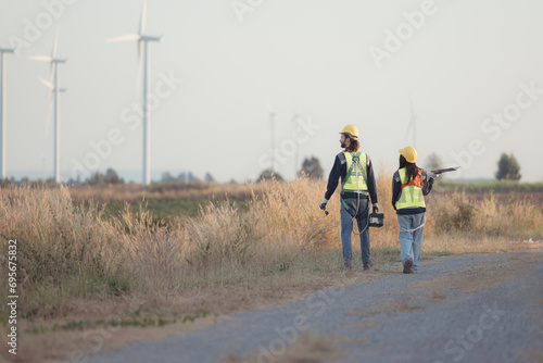 Engineer and worker discussing on a wind turbine farm with laptop