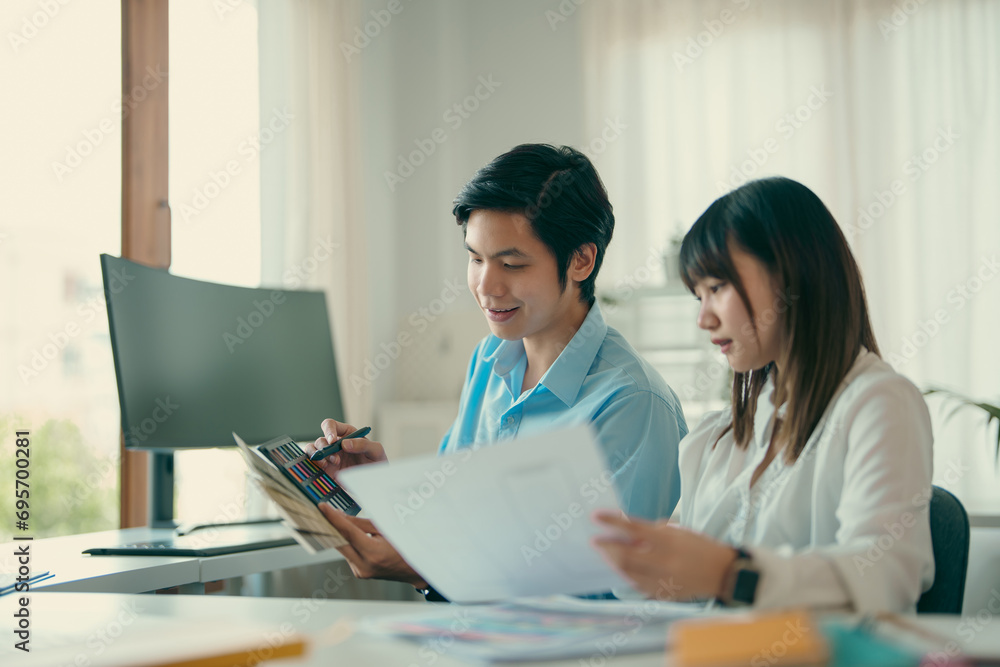 Two young Asian business people sitting together in the office. Two asian designer talking and development ux app on mobile phone during the meeting in office. Two young Asian business people sitting together in the office. Two asian designer talking and development ux app on mobile phone during the meeting in office.