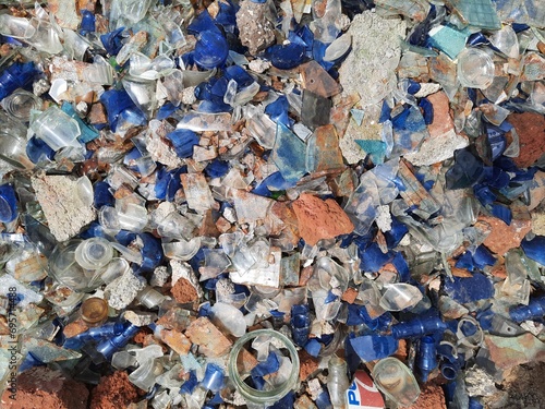 A jumbled mess of shattered glass bottles precariously perched on a mound of dirt, reflecting a chaotic juxtaposition. photo