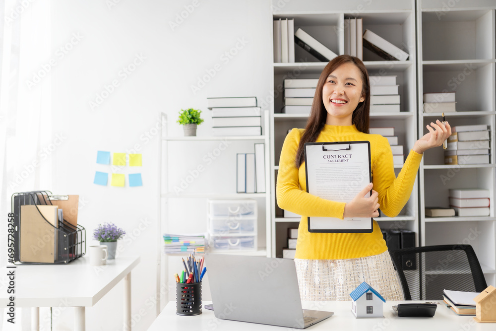Home sales concept, real estate, Asian female employee with small house on table Along with the lease of the sales agreement related to the mortgage loan and home insurance offers.
