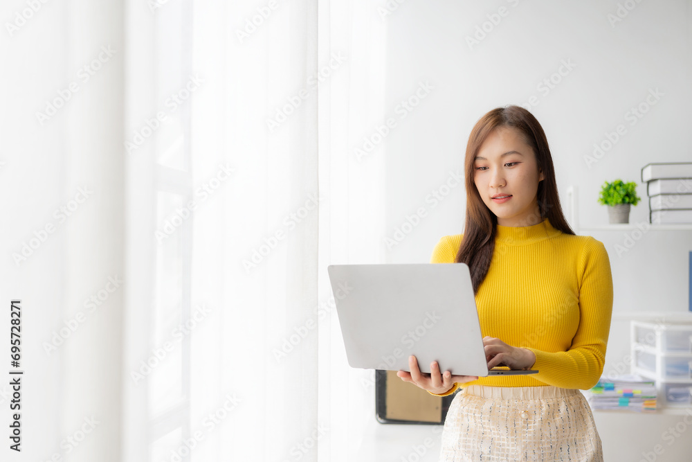 Asian girl holding laptop working in office, standing next to window with mirror, online working concept Asian girl holding laptop working in office, standing next to window with mirror, online working concept