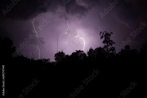 Cloud to ground lightning in the night skies above the silhouetted tree line horizon. 