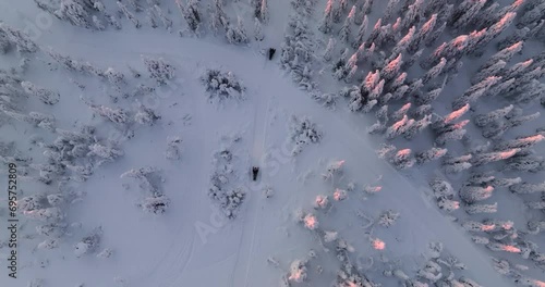 Aerial view following snowmobiles in middle of snowy mountain forest, sunset in Lapland photo