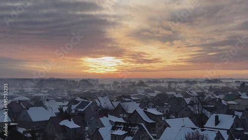Aerial pullback above snow covered suburban roofs with fire yellow sunset streak in sky above misty fog photo