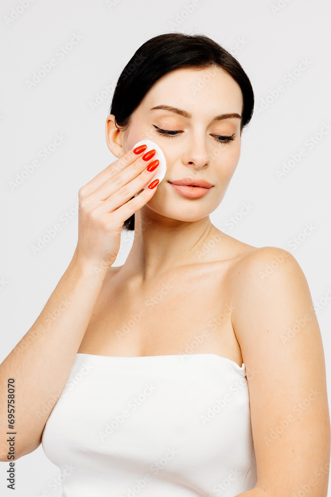 A beautiful young Caucasian woman with brown hair uses a cotton pad. The concept of advertising facial care, cosmetic natural products. A beautiful young Caucasian woman with brown hair uses a cotton pad. The concept of advertising facial care, cosmetic natural products.