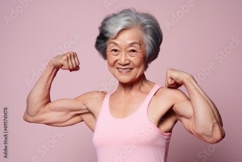 An older woman confidently flexes her muscles against a vibrant pink background. This image can be used to depict strength, fitness, and empowerment
