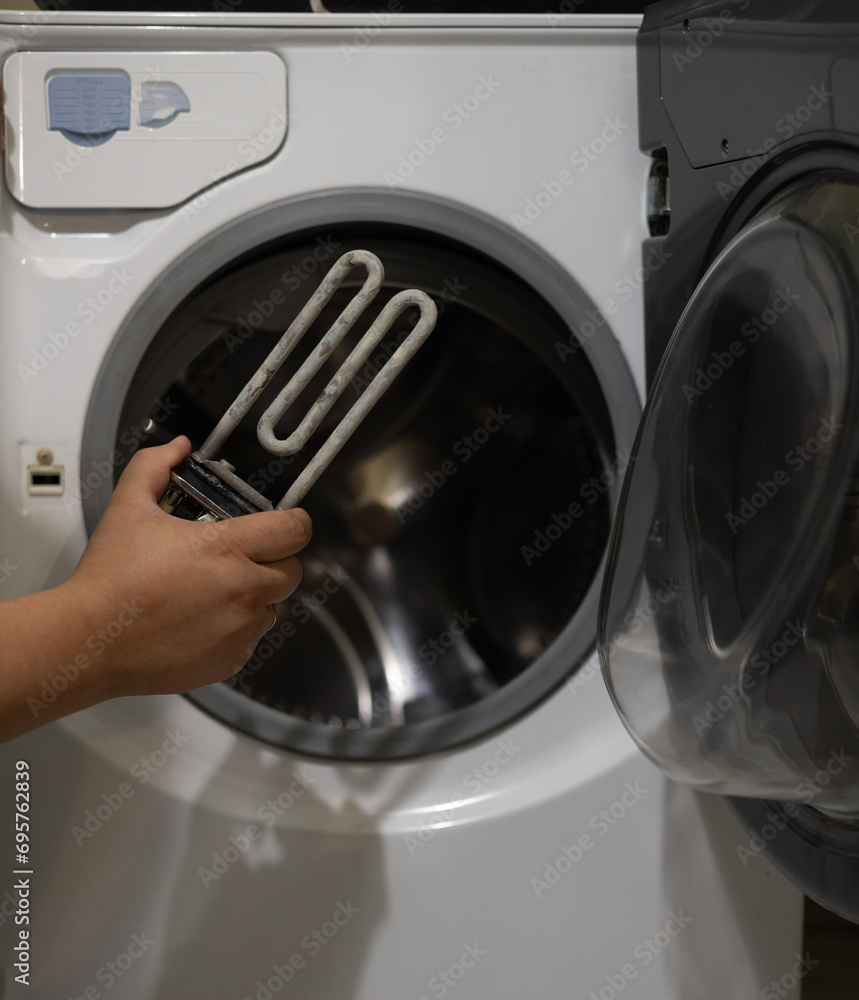 A man examines a heating element with scale against the background of a washing machine. The washing shirt does not work due to a burnt heating element. Washing machine breakdown concept.