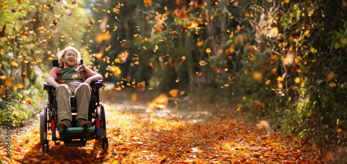 A joyful disabled man sits and rides in a wheelchair on a bright fall day outdoors, surrounded by falling leaves and flying butterflies.Overcoming Self. Strength of spirit.Ultra wide banner.Copy space