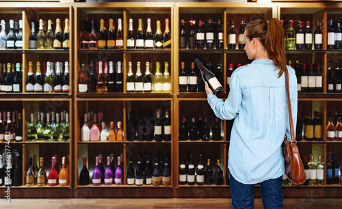 Woman consumer standing in liquor store and choosing wine.  photo