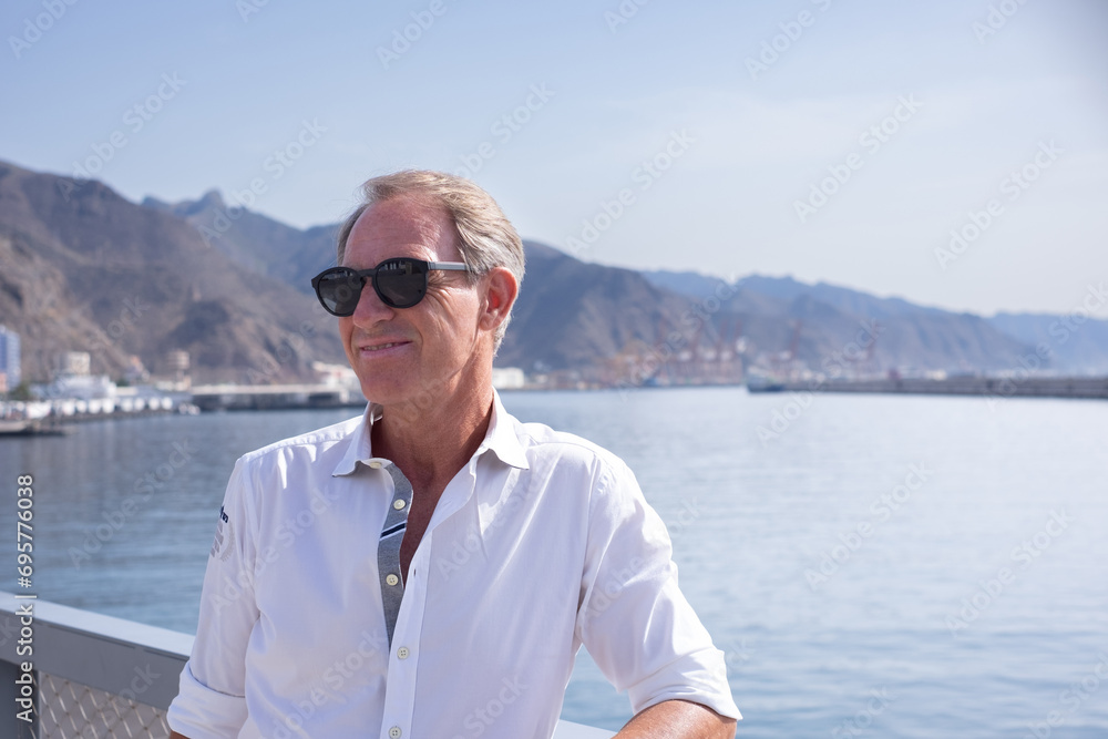 Portrait of handsome middle aged man with sunglasses at sea enjoying outdoors and vacation. Smiling relaxed people in white shirt looking away Portrait of handsome middle aged man with sunglasses at sea enjoying outdoors and vacation. Smiling relaxed people in white shirt looking away