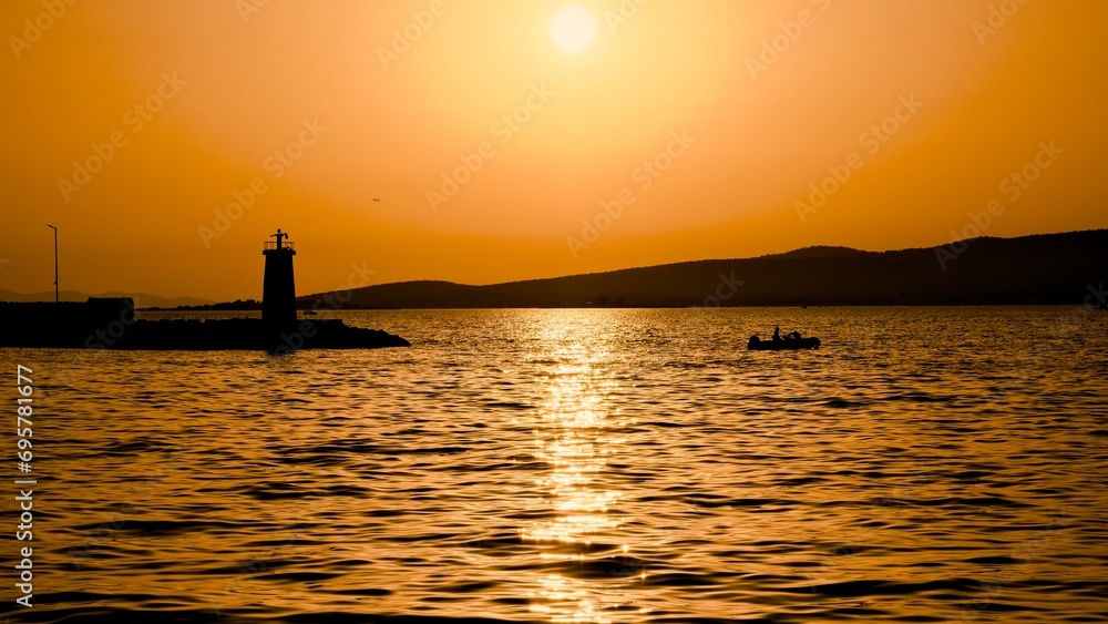 Sunset at sea with lighthouse and fishing boat.