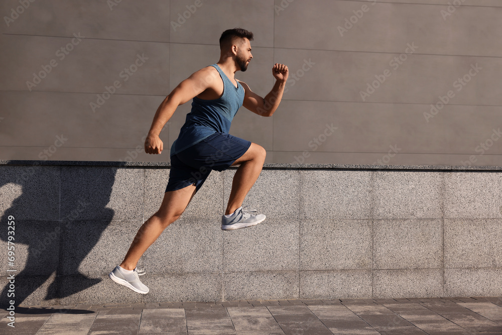 Fototapeta premium Young man running near building outdoors. Space for text