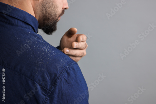 Man brushing dandruff off his shirt on grey background, closeup. Space for text photo
