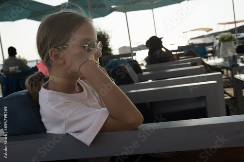 Ritratto di una bambina di nove anni seduta su una poltrona con occhiali da sole e capelli legati. photo