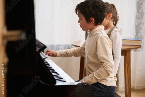 Handsome kids a teenage boy and little child girl, playing grand piano together during a music lesson at home.