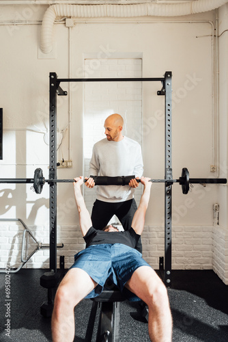 Unrecognizable sportsman on bench exercising with barbell with adult man instructor