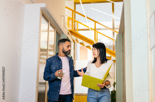 Multiracial coworkers talking reviewing and analyzing company reports in office corridor having coffee