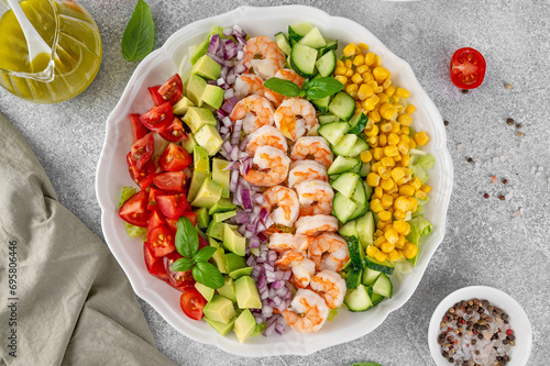 Shrimp salad with vegetables and olive oil mustard dressing. Fresh seafood salad on a white plate on a gray concrete background. Healthy food. Copy space.