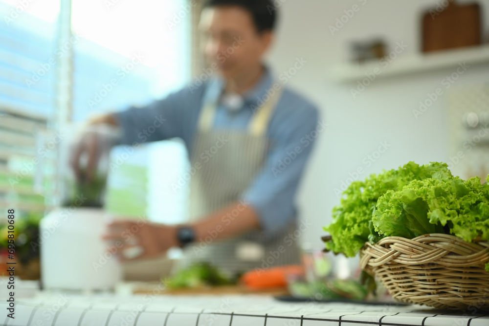 Fresh vegetables in basket on kitchen table with senior man cooking in background. Healthy lifestyle concept Fresh vegetables in basket on kitchen table with senior man cooking in background. Healthy lifestyle concept