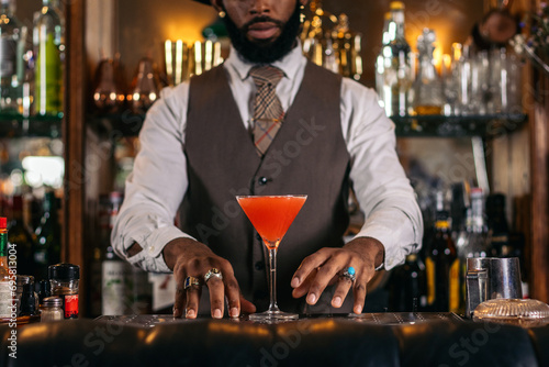 Cutout of a black bartender offering a cocktail served in a martini glass in a traditional cocktail bar