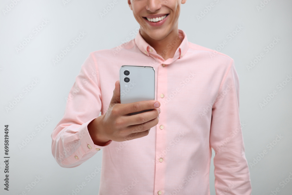 Young man sending message via smartphone on light grey background, closeup Young man sending message via smartphone on light grey background, closeup