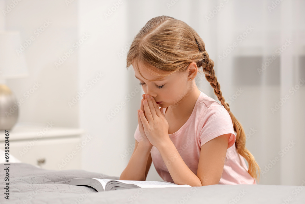 Girl holding hands clasped while praying over Bible in room Girl holding hands clasped while praying over Bible in room