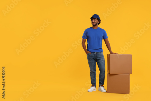 Happy courier with parcels on orange background, space for text