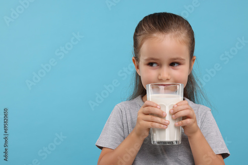 Cute girl with glass of fresh milk on light blue background, space for text