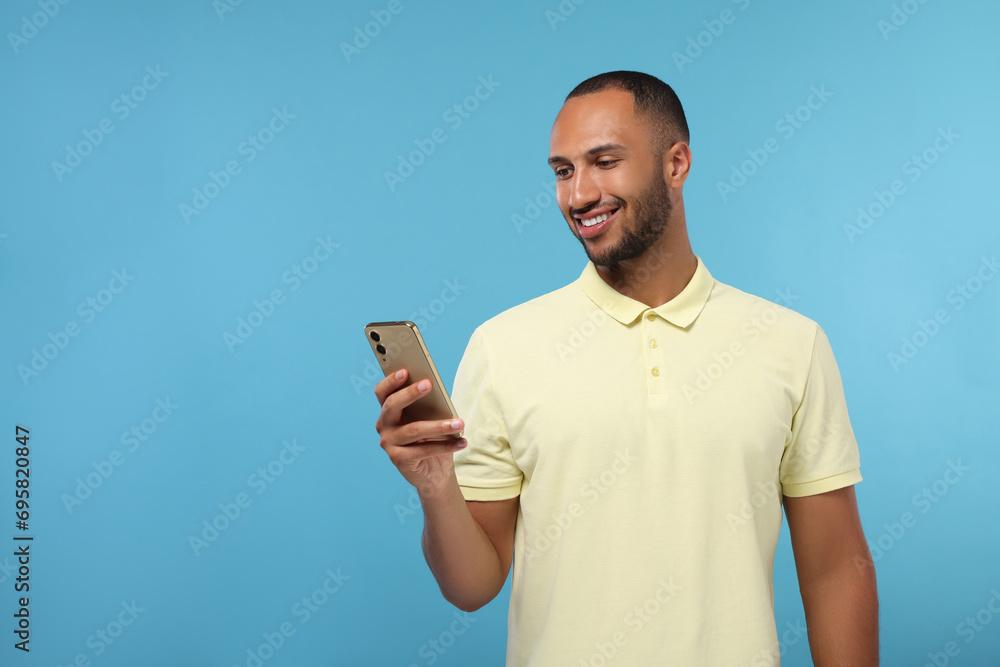 Happy man sending message via smartphone on light blue background, space for text Happy man sending message via smartphone on light blue background, space for text