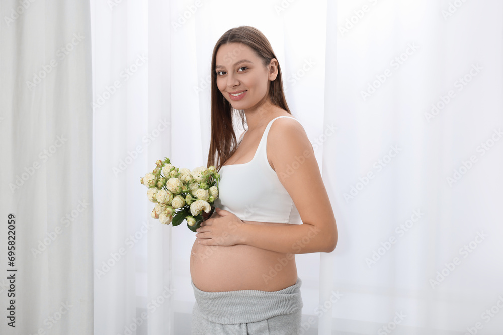 Beautiful pregnant woman with bouquet of roses near window indoors Beautiful pregnant woman with bouquet of roses near window indoors