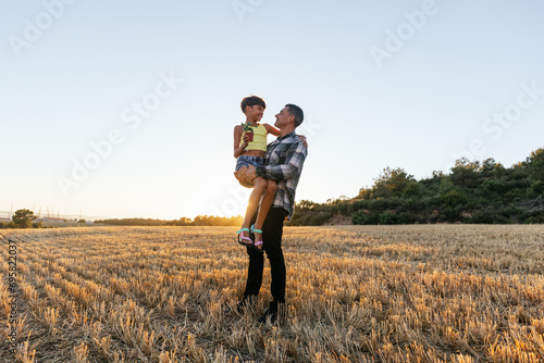 Loving father carries his daughter as they spend time together in the field.