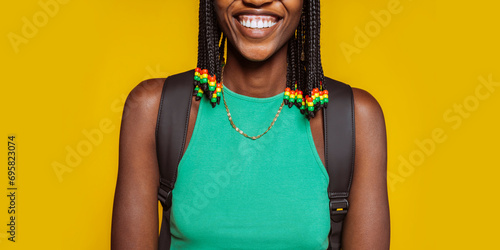Close up portrait of a happy smiling young african american woman in green top, braids and backpack at studio isolated over yellow background. No face. photo