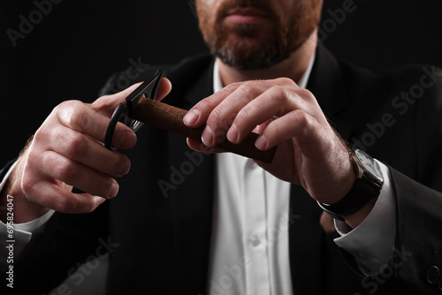 Man cutting tip of cigar on black background, closeup