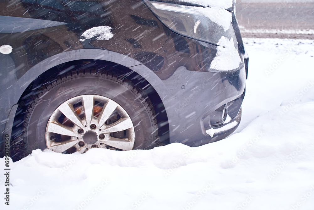 Сar wheel trapped in deep snow. Parked car on snowy side of city road during snow storm.