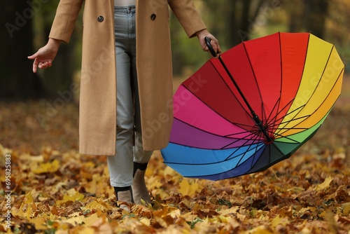 Woman with rainbow umbrella walking in autumn park, closeup