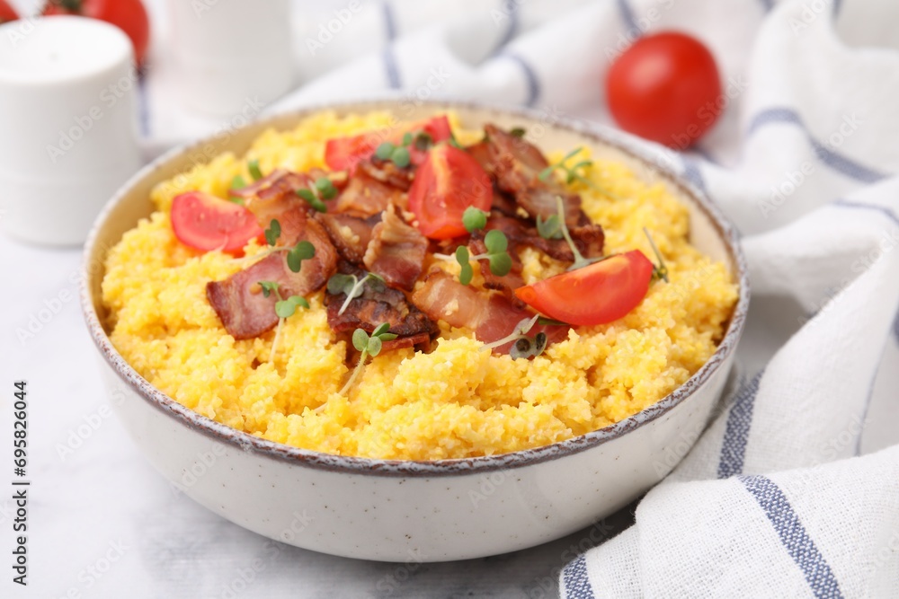 Tasty cornmeal with tomatoes, bacon and microgreens in bowl on white table, closeup