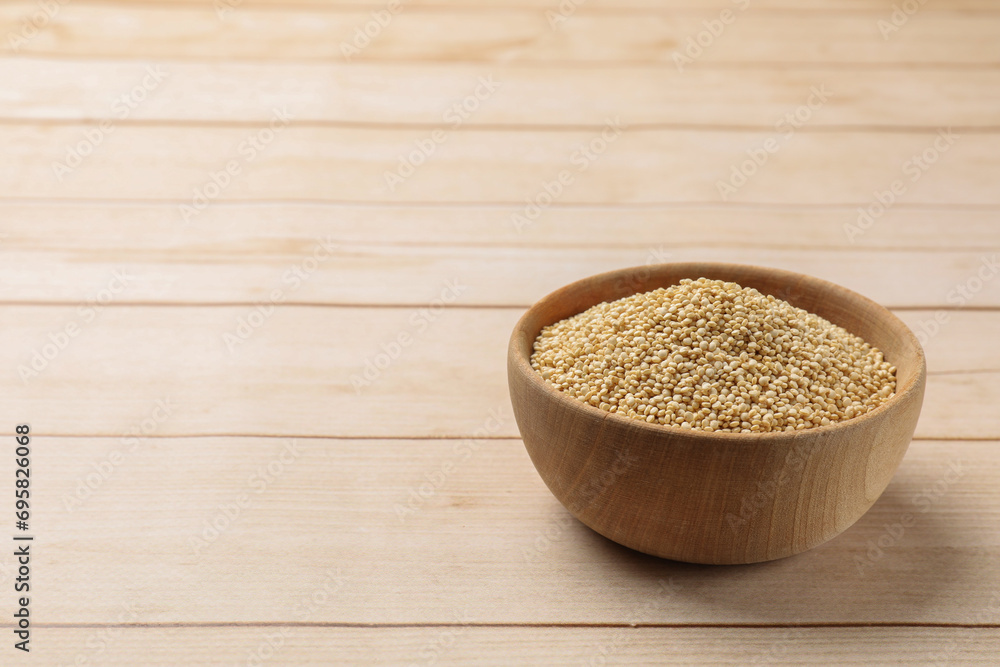Raw quinoa in bowl on wooden table, space for text Raw quinoa in bowl on wooden table, space for text
