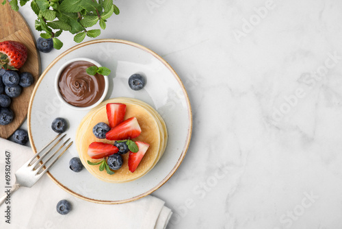 Delicious pancakes with strawberries, blueberries, mint and chocolate sauce served on light marble table, flat lay. Space for text