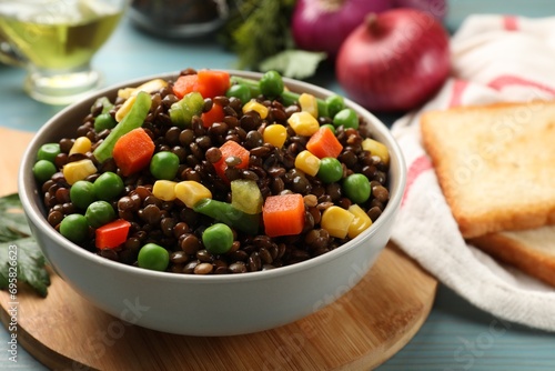 Delicious lentils with vegetables in bowl on light blue table, closeup