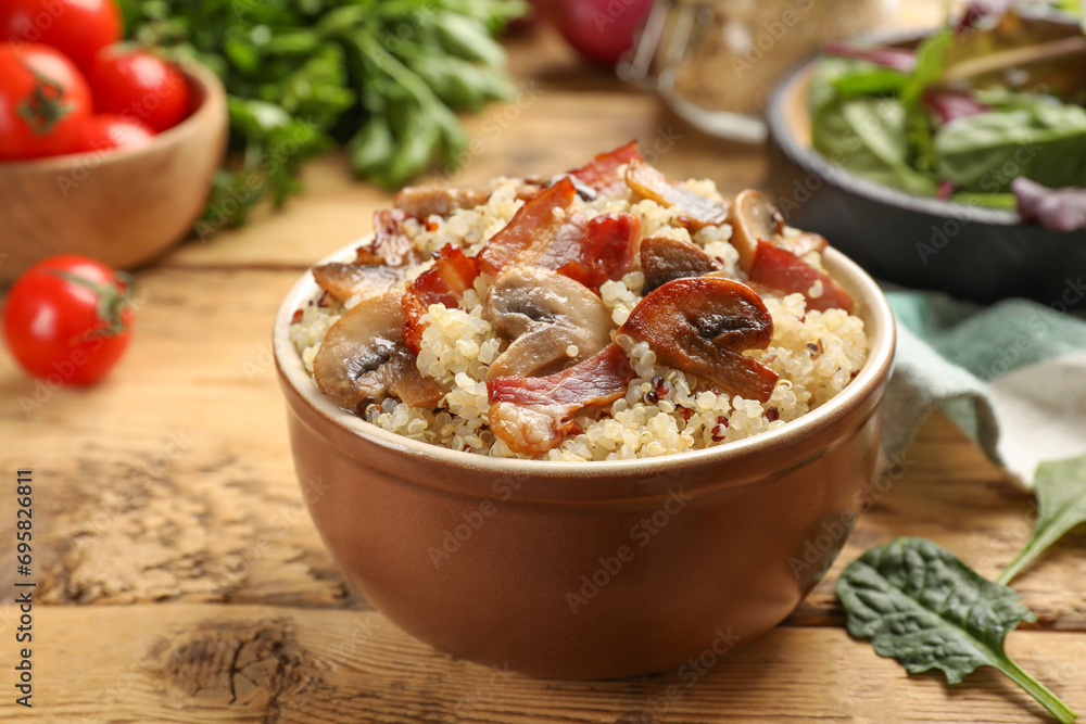 Tasty quinoa porridge with fried bacon and mushrooms in bowl on wooden table, closeup Tasty quinoa porridge with fried bacon and mushrooms in bowl on wooden table, closeup