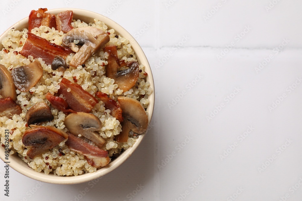 Tasty quinoa porridge with fried bacon and mushrooms in bowl on white tiled table, top view. Space for text Tasty quinoa porridge with fried bacon and mushrooms in bowl on white tiled table, top view. Space for text