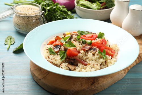 Plate of tasty quinoa porridge with fried bacon, mushrooms and vegetables on light blue wooden table, closeup