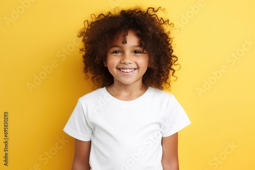 Child girl on a yellow background. A girl smiles at the camera in a white T-shirt. © Viktoria