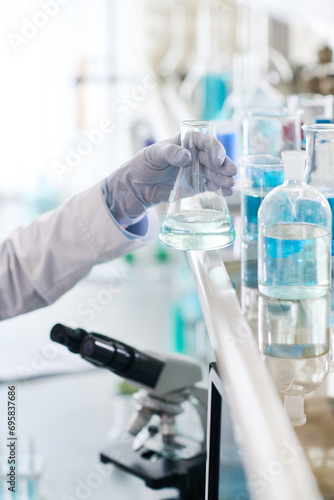 Vertical close up shot of laboratory employees hand in glove holding medical conical flask with liquid